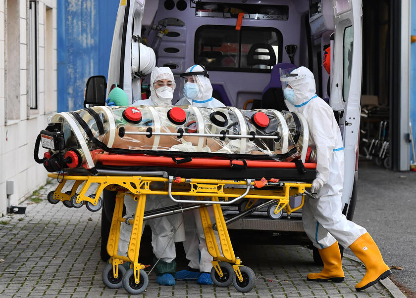 Gli operatori sanitari con le tute protettive trasferiscono un paziente infetto da COVID-19